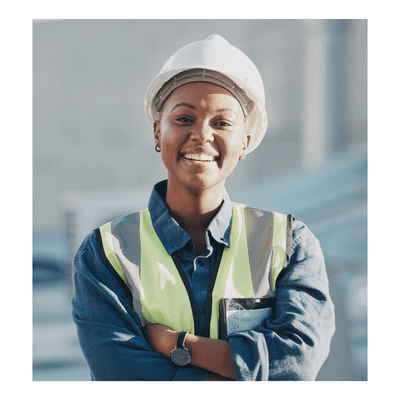 A woman standing in front of a industrial site smiling with a construction hat on